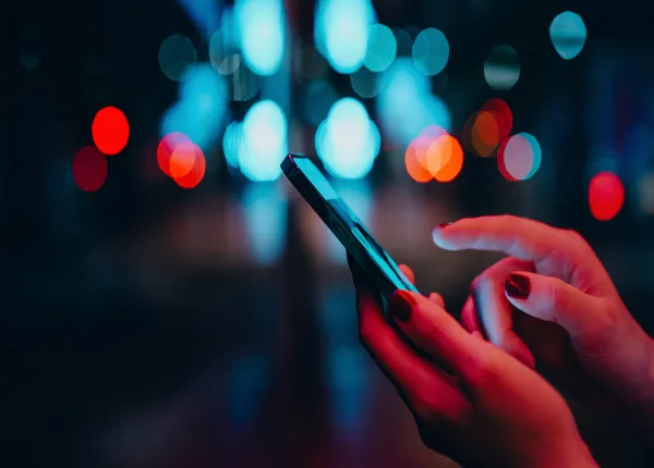 Woman's hands using smartphone in city street at night.