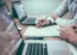 Two people work on a paper document surrounded by laptops.