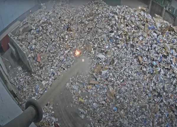 Screenshot from a YouTube video showing a lithium-ion battery fire sparking inside a a dense area of scrap metal and other objects.